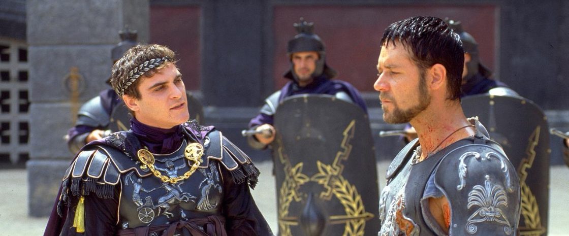 Joaquin Phoenix as Commodus and Russell Crowe as Maximus in a tense scene from Gladiator (2000), wearing Roman armor with guards and shields in the background.