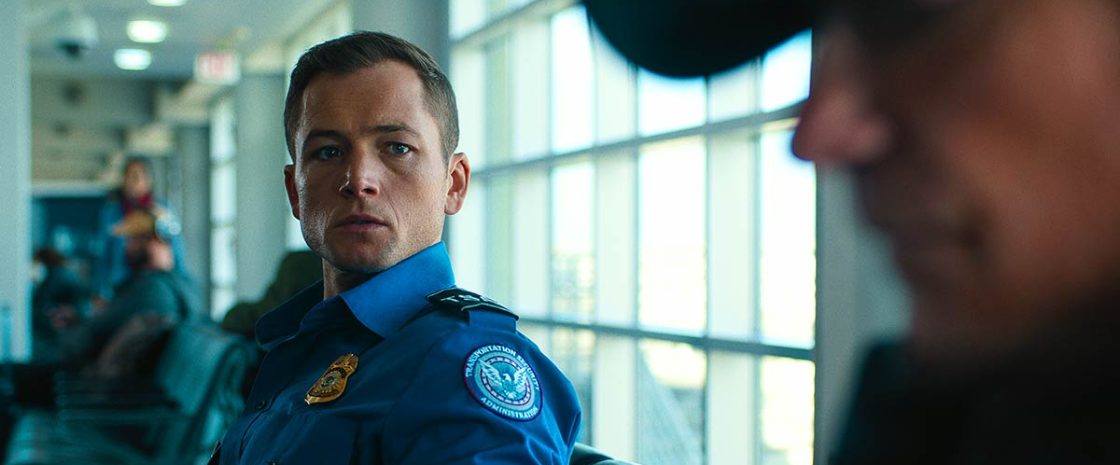 Taron Egerton as a TSA agent in Netflix’s Carry-On, sitting in an airport terminal with a tense expression.